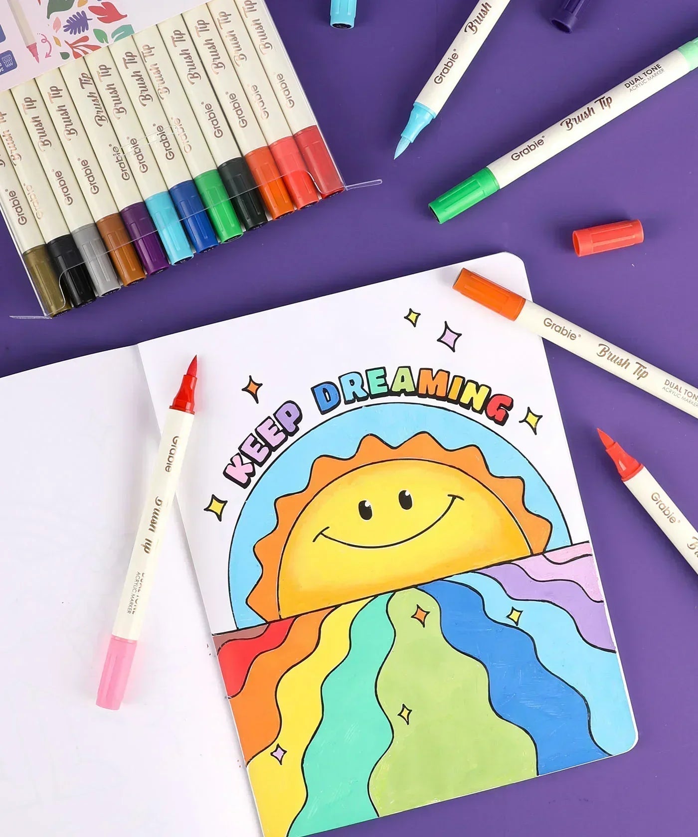 Dual Tone Brush Tip Acrylic Paint Marker Set With Coloring Book showing colorful sun artwork and markers on purple background