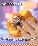 Hand squeezing a soft realistic pastry-shaped Grabie Ultimate Stress Relief Squishy with colorful blurred background.
