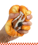 Hand squeezing a realistic croissant-shaped Grabie Ultimate Stress Relief Squishy with icing and raisin details.