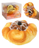 Hand squeezing a dessert-shaped Grabie Ultimate Stress Relief Squishy resembling a bun with icing and a cherry on top.