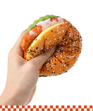 Hand squeezing a realistic burger-shaped Grabie Ultimate Stress Relief Squishy with sesame seed bun and toppings