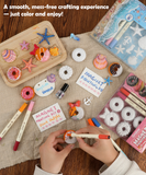 Hands painting colorful seashell and donut magnets with markers beside Magnet Painting Kit (DIY Refrigerator Magnet Kit) packaging and supplies