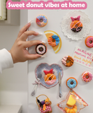 Hand placing colorful donut-shaped magnet on fridge with other decorative magnets and note from Magnet Painting Kit (DIY Refrigerator Magnet Kit)